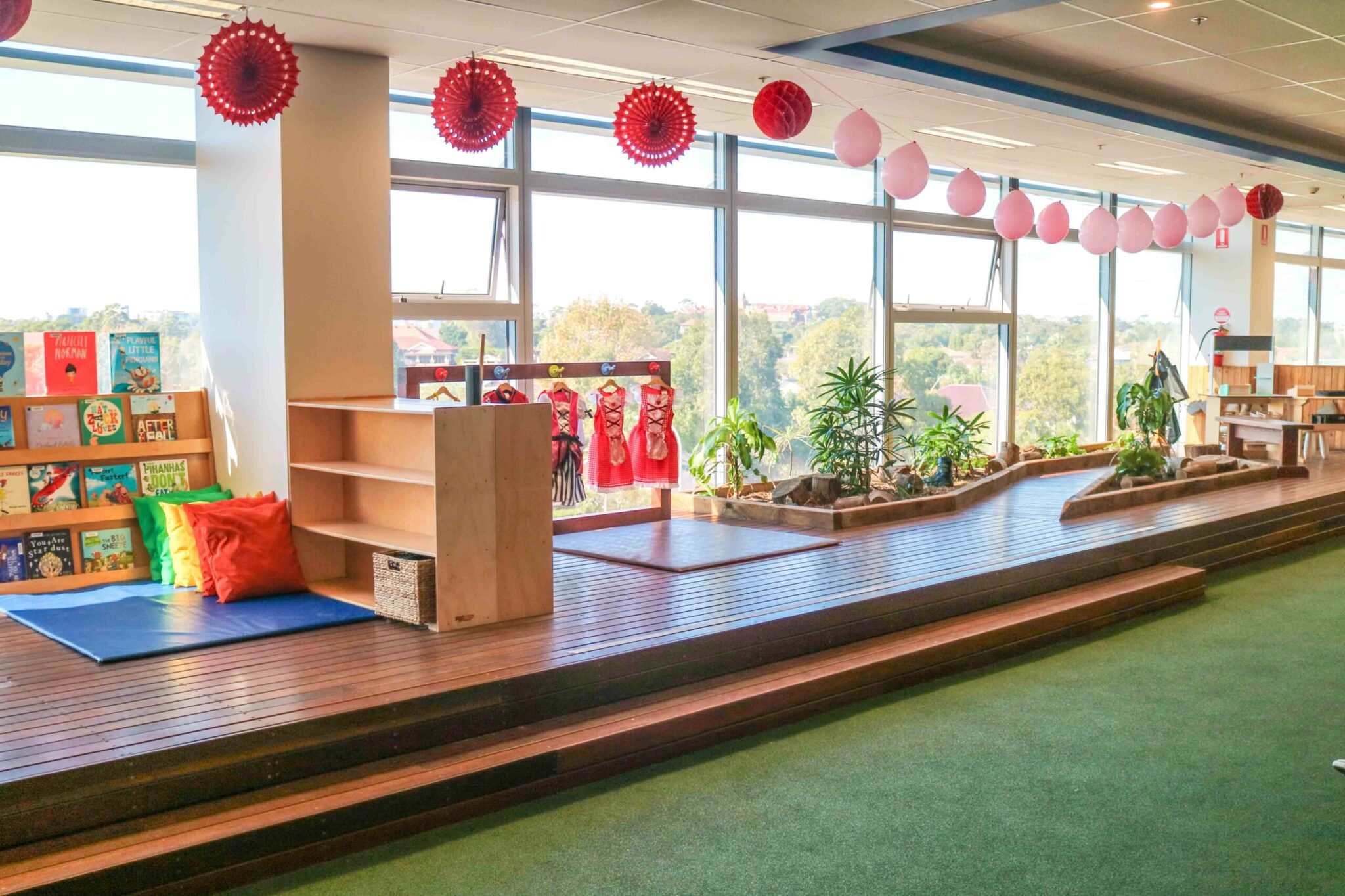 Indoor play area with turf, wood decking, books on shelves and a stunning outdoor view at Victoria Park Montessori Academy.