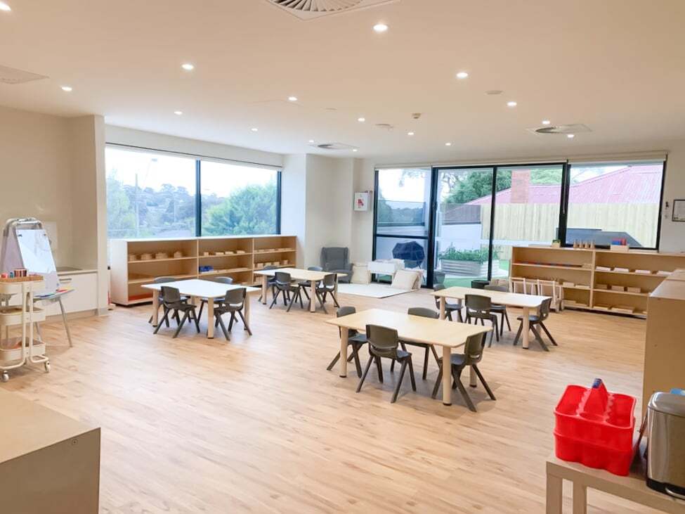 Interior of Montessori Academy’s Box Hill Childcare Centre, with four small classroom tables, a whiteboard, and spacious shelves.