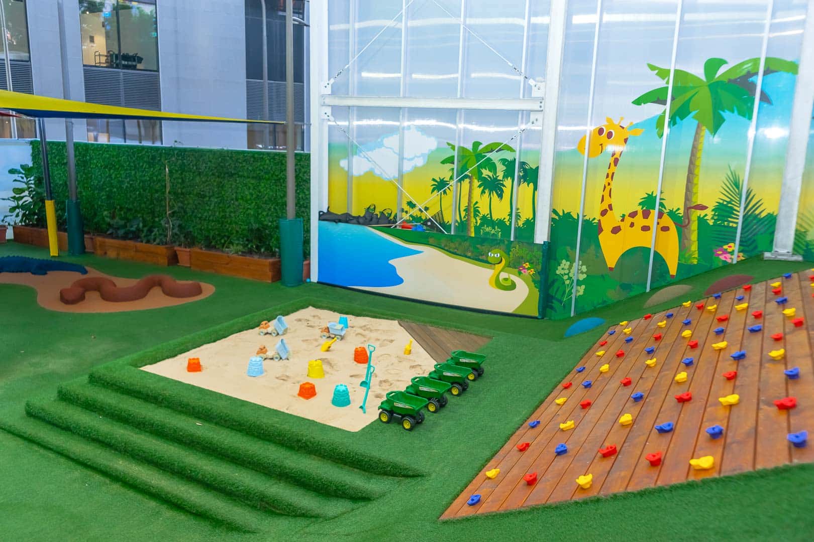 Turfed outdoor play area at Barangaroo Montessori Academy, with a sand pit and climbing wall.