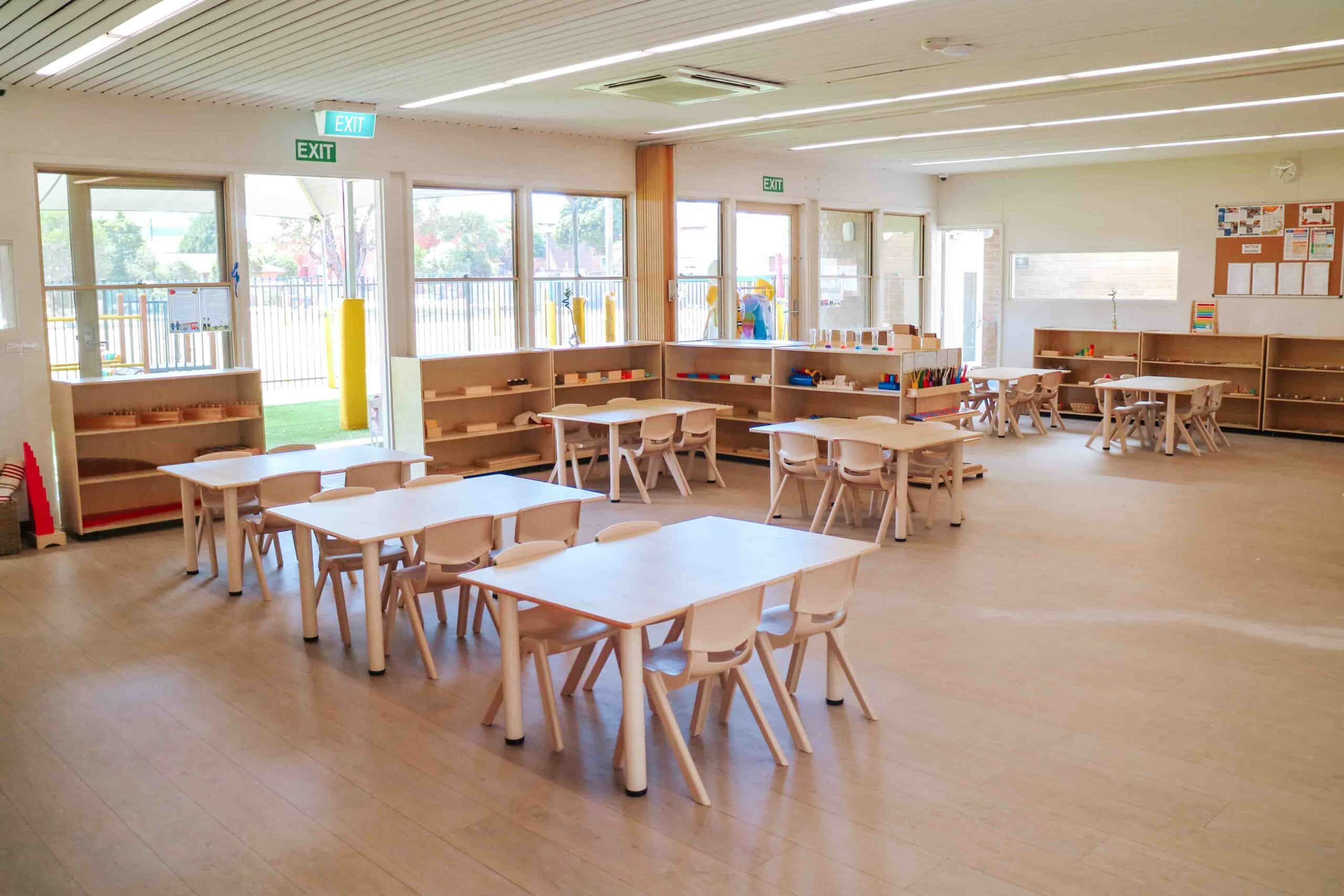 Childcare Montessori Preschool Classroom with open shelving, desks and chairs, and Montessori materials.