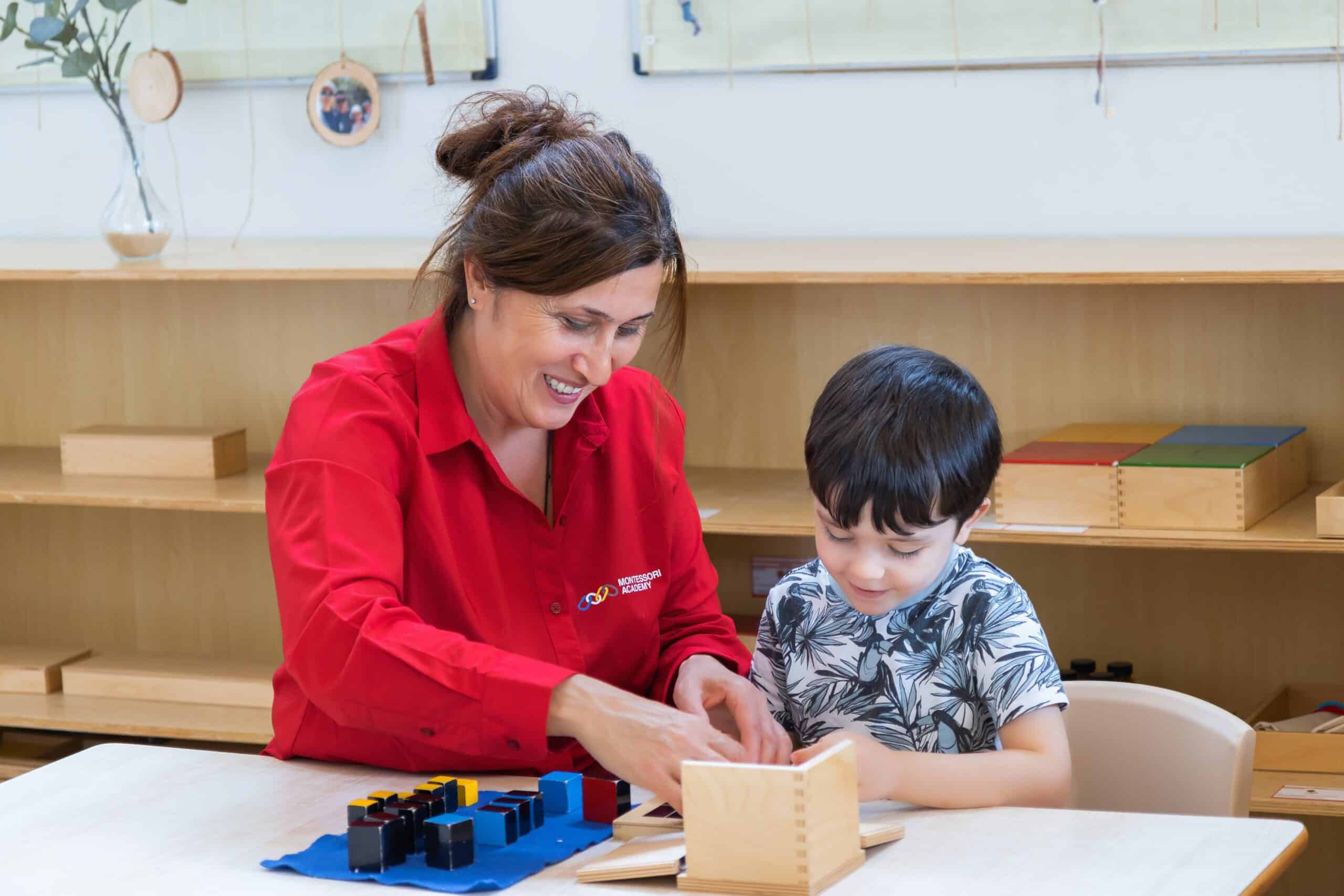 Childcare educator and young boy seated at a table engaged in a learning activity with educational materials.