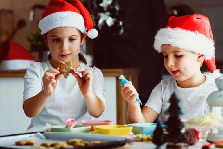 Two children in Santa hats decorating star shaped cookies