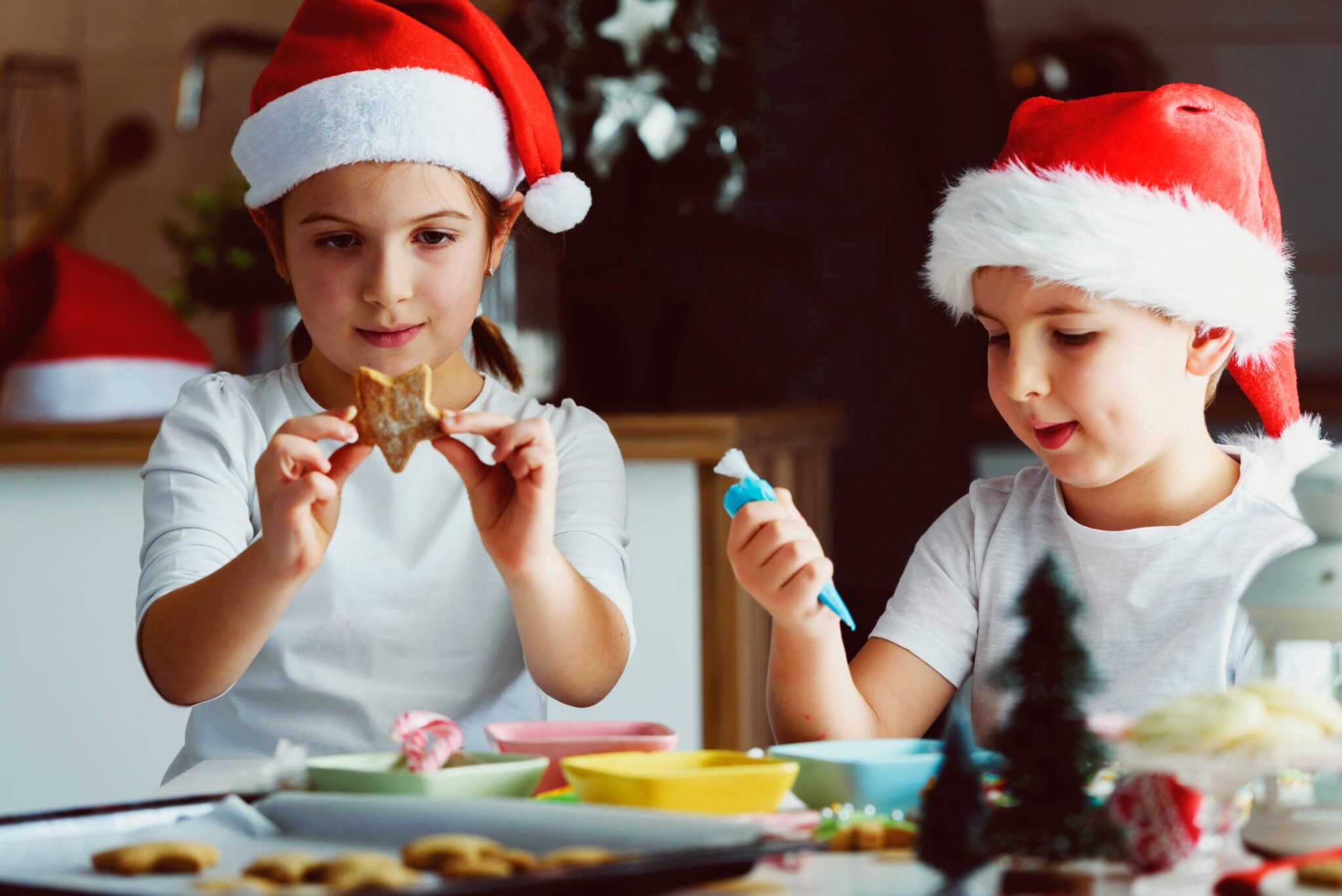 Two children in Santa hats decorating star shaped cookies