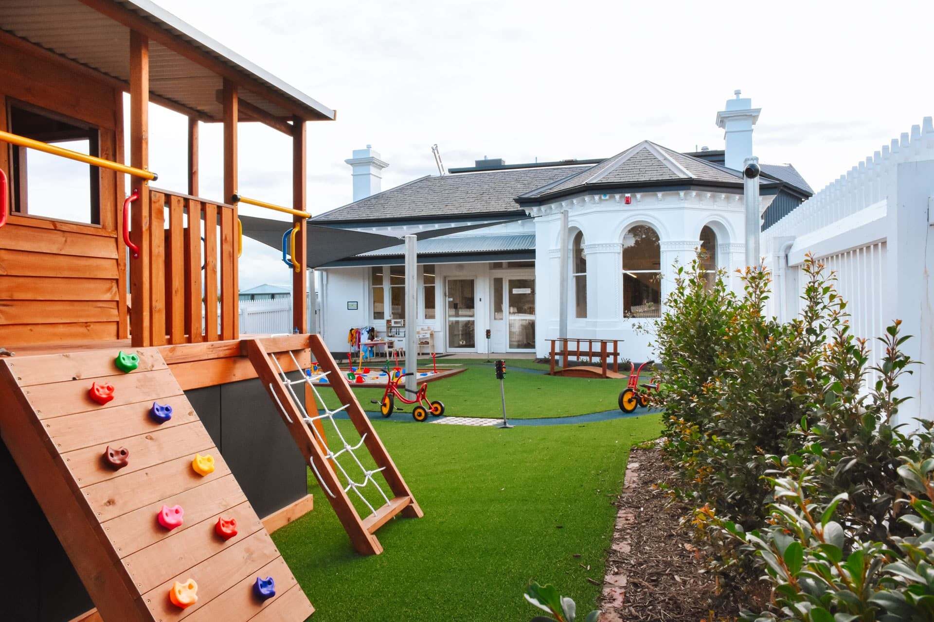 Outdoor playground with climbing ramp, playhouse, play areas, sand pit and bike track at Elsternwick Montessori Academy.
